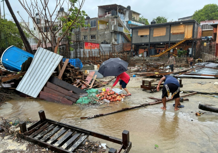 Des habitants marchent parmi les débris laissés au passage de l'ouragan Erick à Puerto Escondido, dans l'Etat du Oaxaca, dans le sud du Mexique, le 19 juin 2025. ( AFP / CARLO ECHEGOYEN )
