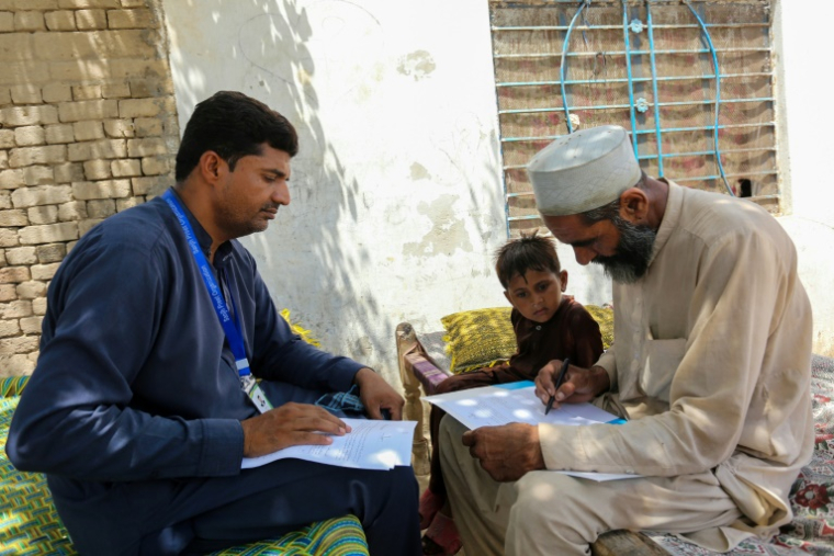 Un bénévole de l'Unicef (g) recueille des données familiales auprès d'un habitant pour aider à l'enregistrement du certificat de naissance de son enfant dans la province du sud-ouest du Pendjab, le 15 mai 2025 au Pakistan ( AFP / Shahid Saeed MIRZA )