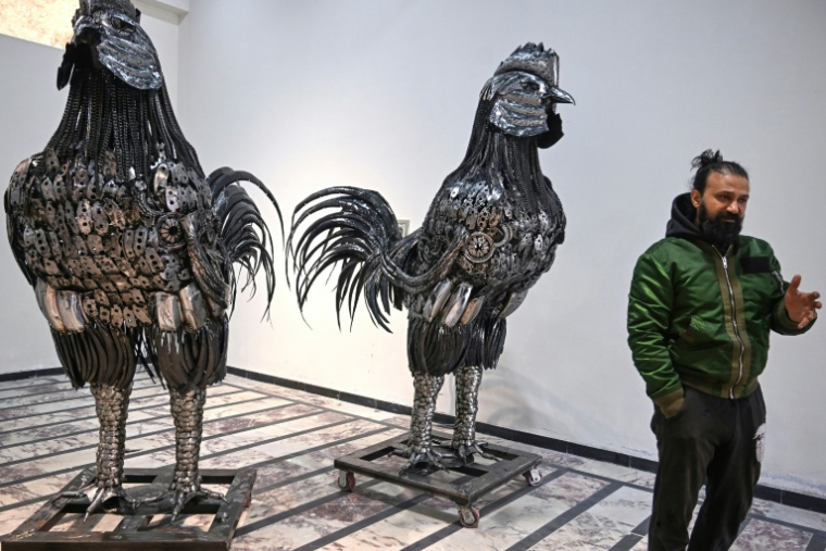 Le sculpteur Ehtisham Jadoon à côté de sculptures de coqs fabriquées à partir de ferraille, dans son atelier situé à la périphérie d'Islamabad, le 29 décembre 2025 au Pakistan ( AFP / Farooq NAEEM )