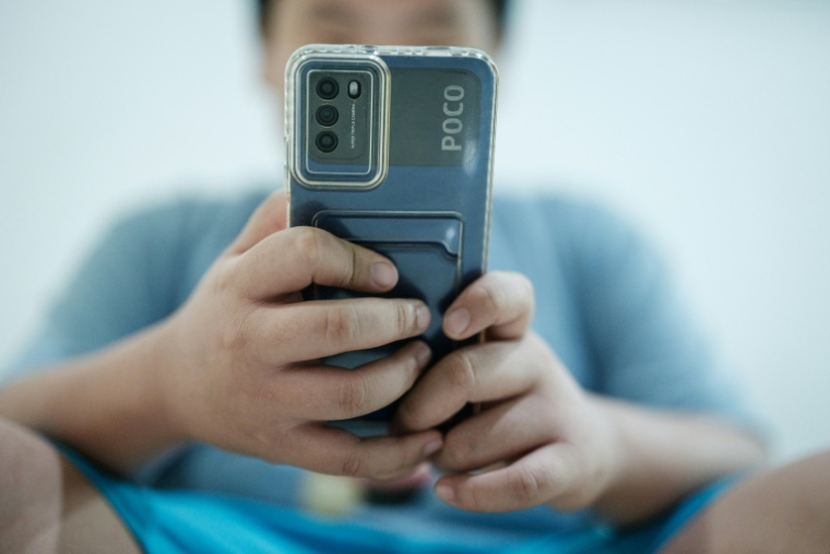 Un petit garçon regarde une vidéo sur son smartphone en attendant son père, à Jakarta, le 25 mars 2026 ( AFP / YASUYOSHI CHIBA )