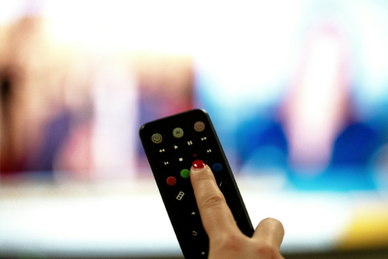 Une personne tient une télécommande pointée vers un écran de télévision, à Paris le 15 janvier 2025 ( AFP / Anna KURTH )