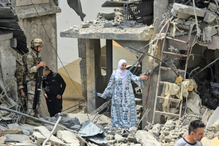 Une femme se fraye un chemin à travers les décombres sous le regard d'un soldat libanais, sur le site d'un immeuble résidentiel touché la veille par une frappe israélienne près de la ville de Burj al-Shamali, au sud de Tyr, le 27 mai 2026 ( AFP / KAWNAT HAJU )