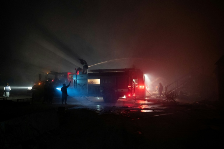 Des pompiers afghans et des agents de sécurité talibans travaillent sur le site d'un incendie après des frappes pakistanaises, le 16 mars 2026 à Kaboul ( AFP / Wakil KOHSAR )