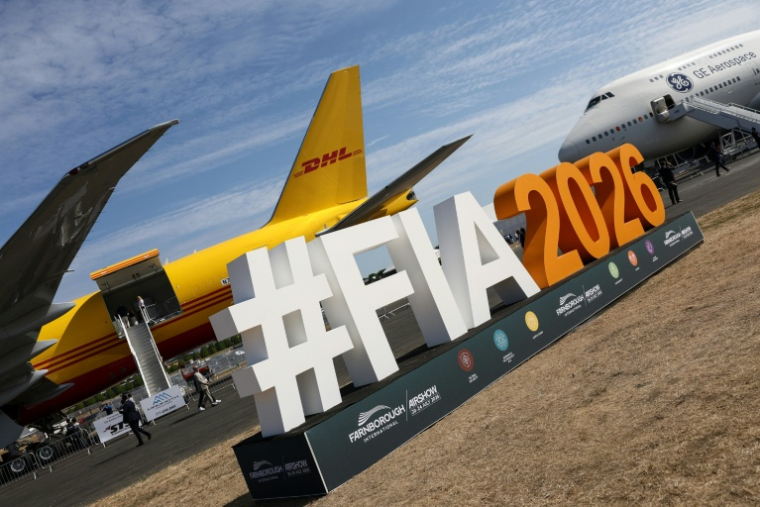 Le logo du salon aéronautique international de Farnborough devant un Boeing 777-200 (g) du géant du transport DHL et un Boeing 747 de GE Aerospace (d), lors de la journée d'ouverture à Farnborough, au sud-ouest de Londres, le 20 juillet 2026 ( AFP / Toby Shepheard )