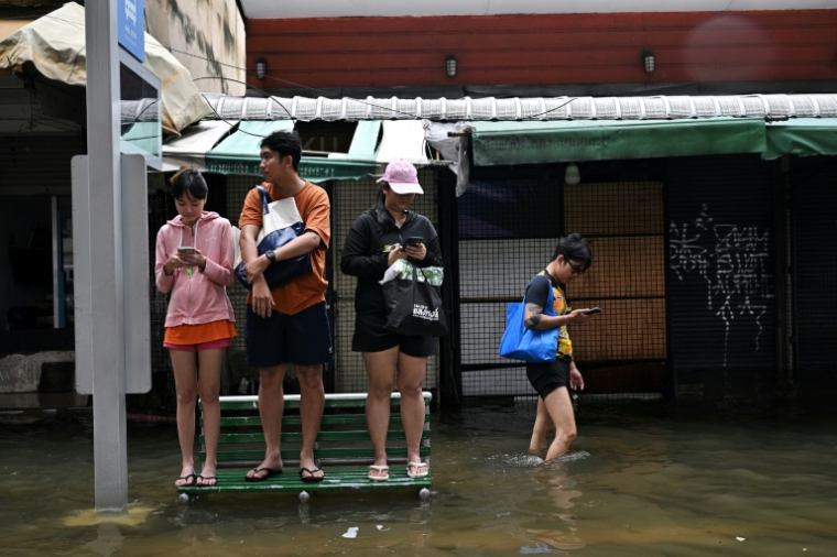 Des habitants sur un banc dans une rue de Bangkok, où l'état de catastrophe naturelle a été déclaré après des pluies diluviennes qui ont inondé habitations, commerces et axes de circulation, le 27 septembre 2026 ( AFP / Lillian SUWANRUMPHA )