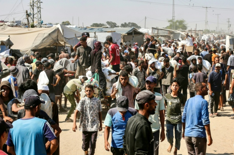 Des Palestiniens portent des sacs d'aide humanitaire après une distribution, à Al-Mawasi, dans le sud de la bande de Gaza, le 27 juillet 2025 ( AFP / - )