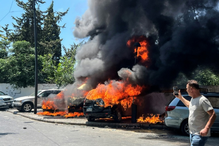 Un homme prend des photos de véhicules en feu après une frappe israélienne, le 10 juin 2026 à Saïda au Liban ( AFP / Mahmoud ZAYYAT )