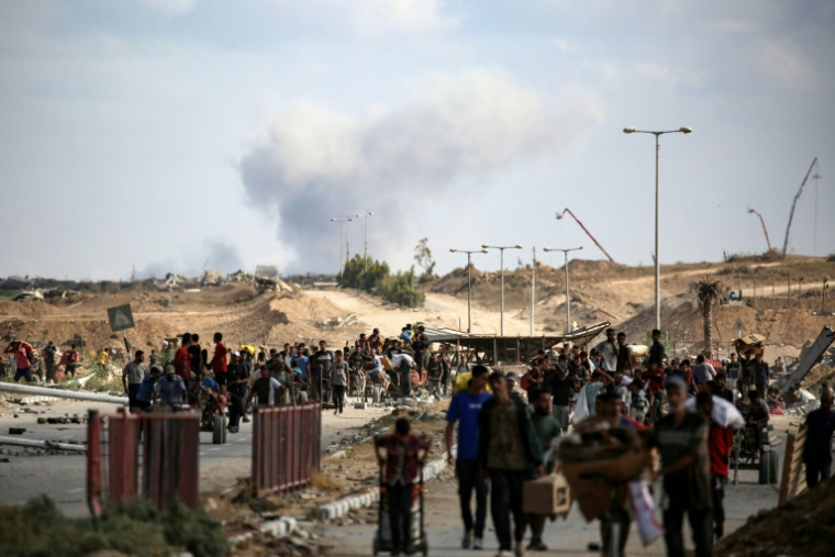 Une colonne de fumée s'élève  en arrière-plan après une frappe alors que des Palestiniens reviennent d'un point de distribution alimentaire dans le centre de la bande de Gaza, le 5 octobre 2025 ( AFP / Eyad BABA )
