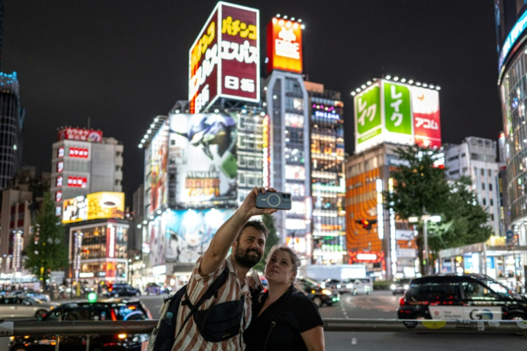 Des touristes font un selfie dans le quartier de Shinjuku, le 11 août 2026 à Tokyo ( AFP / Philip FONG )