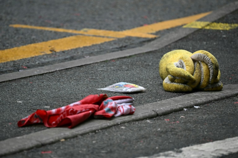 Une peluche et un drapeau de Liverpool gisent sur la chaussée, derrière un cordon de police, sur Water Street à Liverpool, dans le nord-ouest de l'Angleterre, le 27 mai 2025, après qu'une voiture a foncé sur la foule la veille ( AFP / Paul ELLIS )