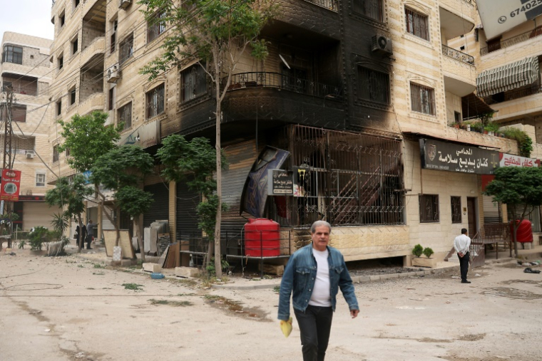 Un homme passe devant un bâtiment partiellement incendié lors de violences impliquant des druzes près de Damas, le 1er mai 2025 ( AFP / OMAR HAJ KADOUR )