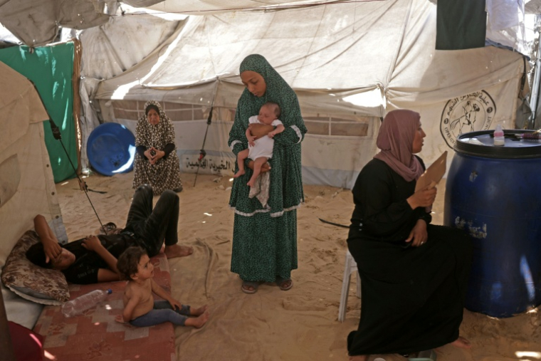 Rouba, petite Palestinienne (à gauche) souffrant de la varicelle, avec des membres de sa famille sous la tente où ils habitent dans le camp de Khan Younes, à Gaza, le 19 juillet 2026 ( AFP / Bashar Taleb )