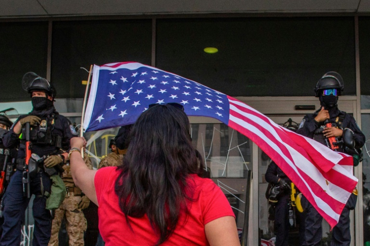 Une manifestante brandit un drapeau américain devant des soldats de la Garde nationale déployés devant les bureaux du gouvernement fédéral à Los Angeles, le 10 juin 2025 ( AFP / Apu GOMES )