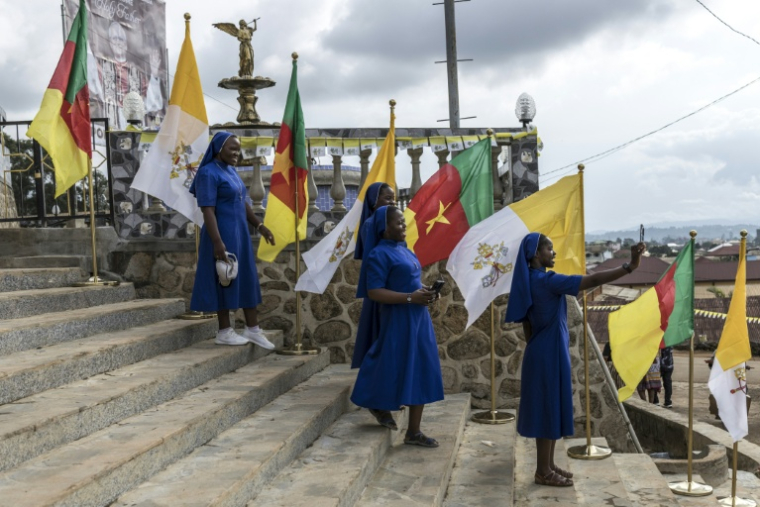 Des religieuses catholiques se prennent en photo à côté des drapeaux camerounais et du Vatican à la cathédrale métropolitaine Saint-Joseph de Bamenda, le 15 avril 2026, à la veille de la visite du pape Léon XIV à Bamenda. ( AFP / PATRICK MEINHARDT )