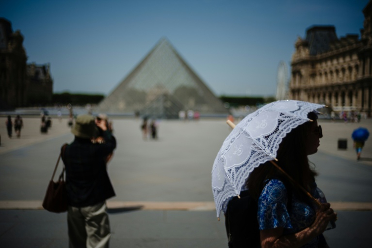 Une touriste se protège du soleil sous une ombrelle devant la pyramide du Louvre conçue par l'architecte sino-américain Ieoh Ming Pei, le 23 juin 2026 à Paris, lors d'un épisode de canicule en France  ( AFP / Dimitar DILKOFF )