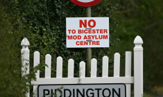 Un panneau indiquant l'entrée du village britannique de Piddington à côté d'un autre sur lequel on peut lire "Non au centre d’accueil pour demandeurs d’asile du ministère de la Défense à Bicester", le 15 septembre 2026 ( AFP / JUSTIN TALLIS )