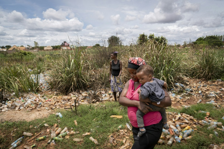 Hélène Mvubu porte sa fille en marchant dans un champ pollué à Lubumbashi en République démocratique du Congo le 24 novembre 2025 ( AFP / Glody MURHABAZI )