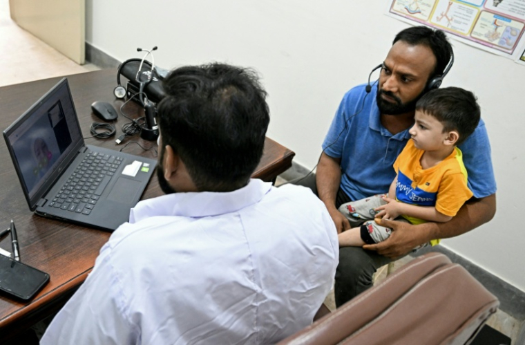 Muhammad Adil (au centre) bénéficie d'une consultation médicale en ligne et gratuite pour son fils, dans une clinique de la société de santé numérique Sehat Kahani à Karachi (Pakistan), le 7 avril 2026 ( AFP / Rizwan TABASSUM )