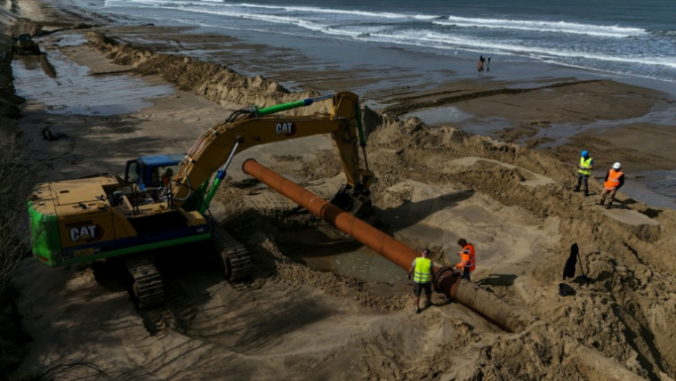 Des ouvriers raccordent une section de tuyau dans le cadre d'une expérimentation de lutte contre l'érosion marine, à Soulac-sur-Mer, en Gironde, le 10 avril 2026 ( AFP / Christophe ARCHAMBAULT )