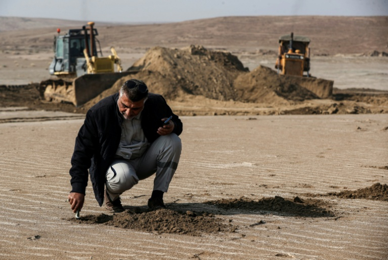 Un ingénieur irakien examine le sol tandis que des bulldozers dégagent des dunes de sable et extraient de l’argile dans le désert au sud de Samawah, le 21 décembre 2025 ( AFP / AHMAD AL-RUBAYE )
