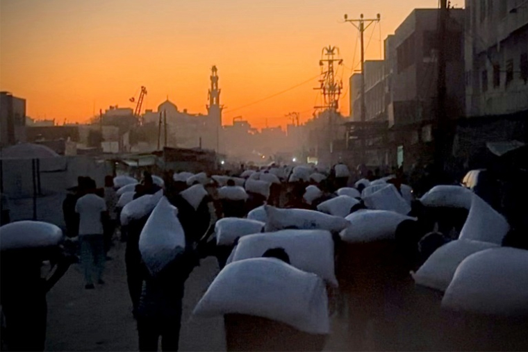 Des Palestiniens marchent en portant des sacs de farine à Khan Younès, dans le sud de la bande de Gaza, le 22 juillet 2025 ( AFP / - )