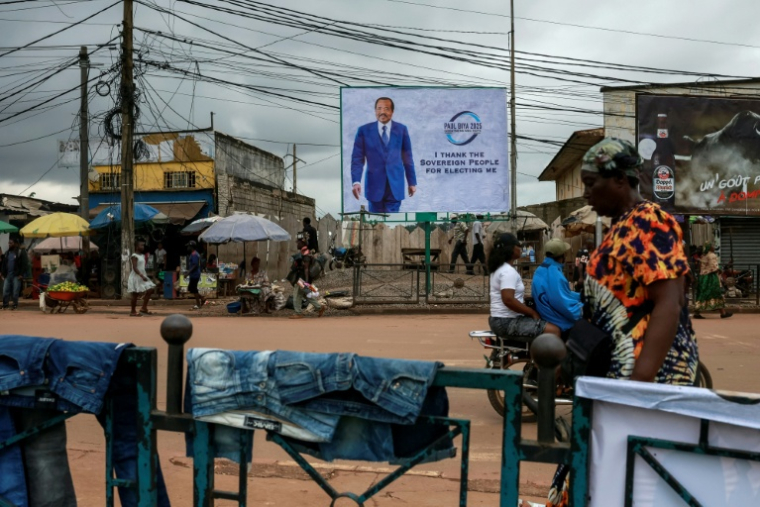 Des piétons passent devant un panneau publicitaire représentant le président camerounais Paul Biya, dans une rue de Yaoundé, le 28 octobre 2025, au lendemain de l'annonce des résultats de l'élection présidentielle au Cameroun.  ( AFP / - )