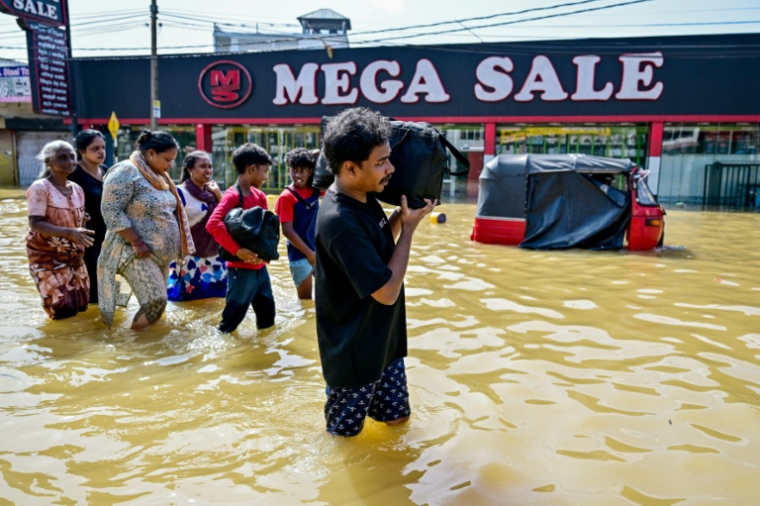 Des victimes des inondations traversent une rue avec leurs affaires, à Wellampitiya, en périphérie de Colombo, le 30 novembre 2025 ( AFP / Ishara S. KODIKARA )