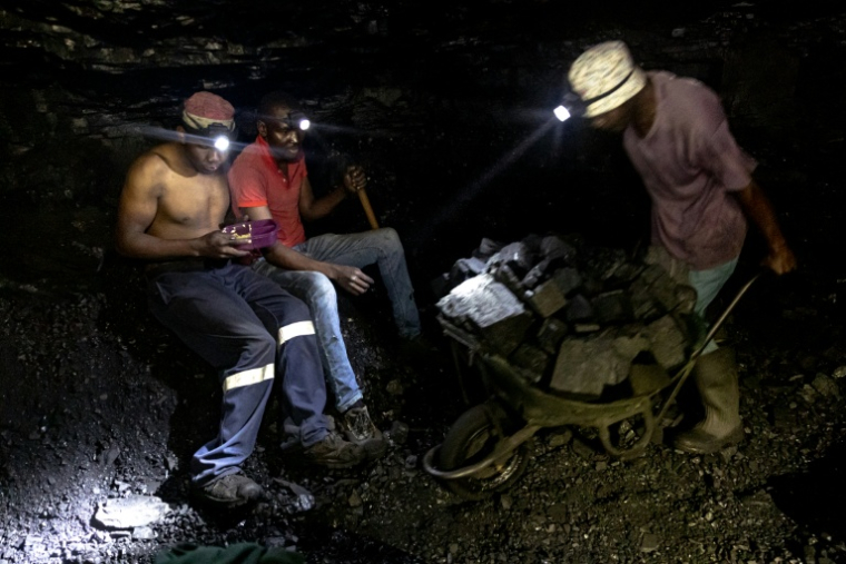 Des mineurs illégaux font une pause tandis qu'un autre pousse une brouette remplie de charbon dans la mine de Golfview à Ermelo le 25 septembre 2025, en Afrique du Sud ( AFP / EMMANUEL CROSET )