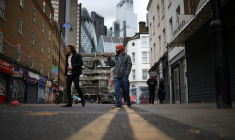 Des personnes passent devant des magasins, avec le quartier financier de la City de Londres en arrière-plan, à Londres, en Grande-Bretagne