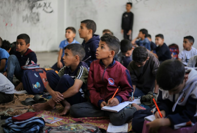Des enfants palestiniens assis par terre écoutent leur institutrice dans le camp de réfugiés de Nousseirat, dans le centre de la bande de Gaza, le 26 octobre 2025 ( AFP / Eyad BABA )