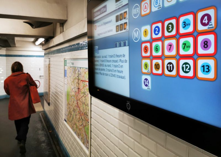 Une femme passe devant un écran d'information affichant la liste des lignes de métro dont le service est interrompu à Paris
