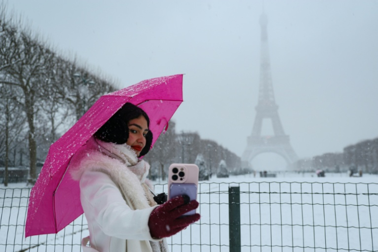 Une femme se prend en photo devant la Tour Eiffel, dans Paris sous la neige, le 5 janvier 2026   ( AFP / Ludovic MARIN )