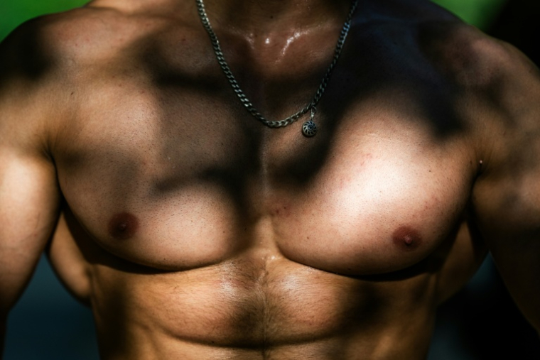 Le torse musclé d'un homme qui s'entraîne sur une aire de street workout à Paris, le 10 août 2025 ( AFP / Julie SEBADELHA )