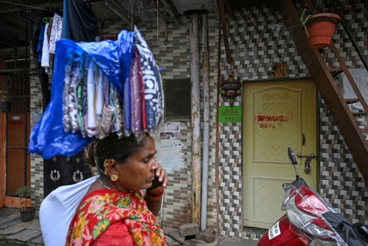 Une vendeuse ambulante passe devant des maisons destinées à être réaménagées dans le cadre d'un projet de rénovation urbaine du bidonville de Dharavi, le 8 juillet 2025 à Bombay, en Inde ( AFP / Indranil MUKHERJEE )