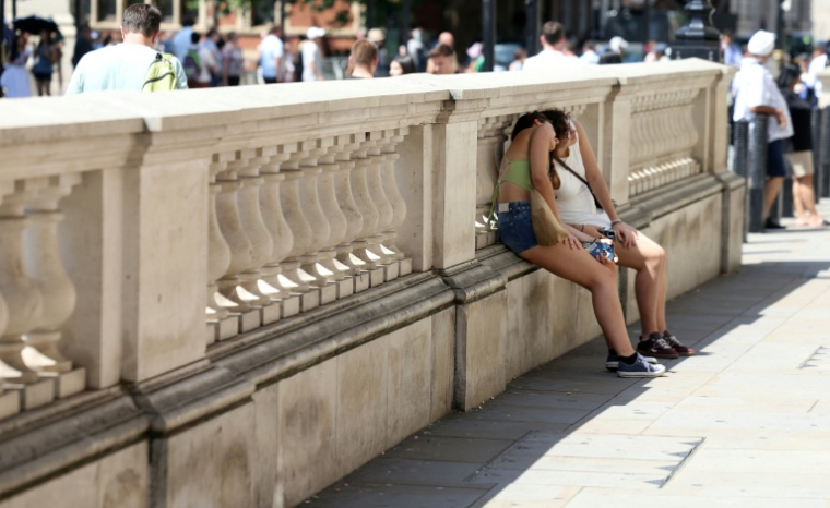 Des personnes se protégent du soleil derrière un mur, le 24 juin 2026 à Londres ( AFP / Toby Shepheard )
