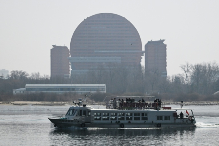 Un bateau touristique chinois sur le fleuve Yalu passe devant un hôtel de la ville nord-coréenne de Sinuiju, face à la ville frontalière de Dandong, dans le nord-est de la Chine, le 26 mars 2026 ( AFP / GREG BAKER )