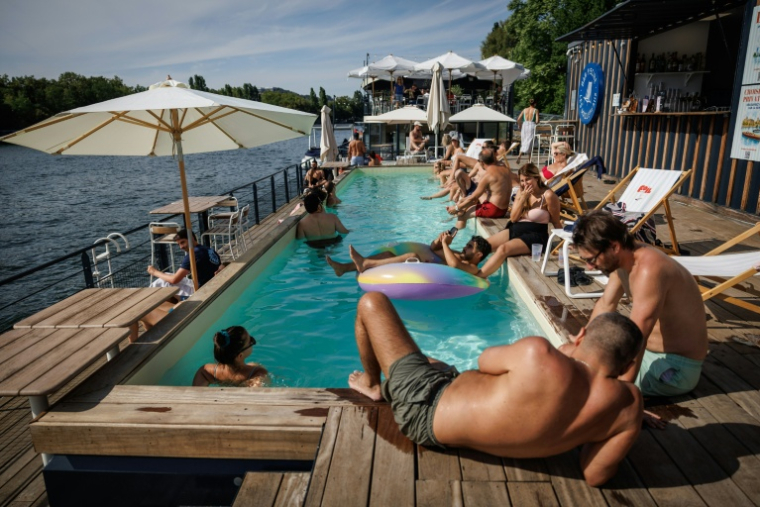 Des clients se prélassent au bord de la piscine de Foil in Paris, en bord de Seine, le 2 août 2026 ( AFP / Simon WOHLFAHRT )