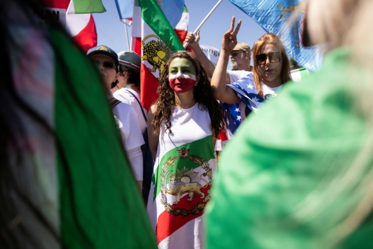 Une manifestante envelopée dans un drapeau utilisé par l'Iran avant la révolution islamique, autour du SoFi Stadium à Inglewood, près de Los Angeles, le 15 juin 2026 ( AFP / ETIENNE LAURENT )