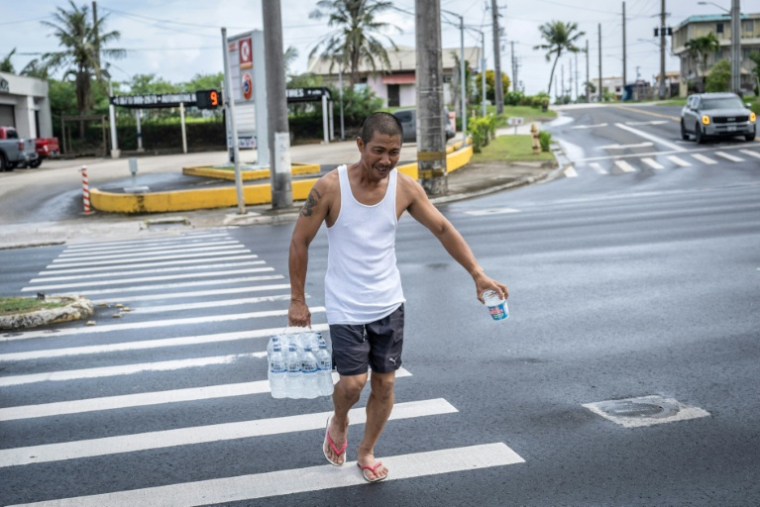 Un homme porte un pack de bouteilles d'eau à Guam alors que le typhon Bavi approche de l'île américaine du Pacifique le 5 juillet 2026 ( AFP / Yuichi YAMAZAKI )