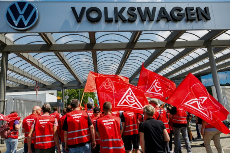 Des salariés de Volkswaggen, portant des drapeaux d'IG Metall, protestant contre le plan de restructuration préparé par la direction, à Zwickau, le 9 juillet 2026 ( AFP / Jens SCHLÜTER )