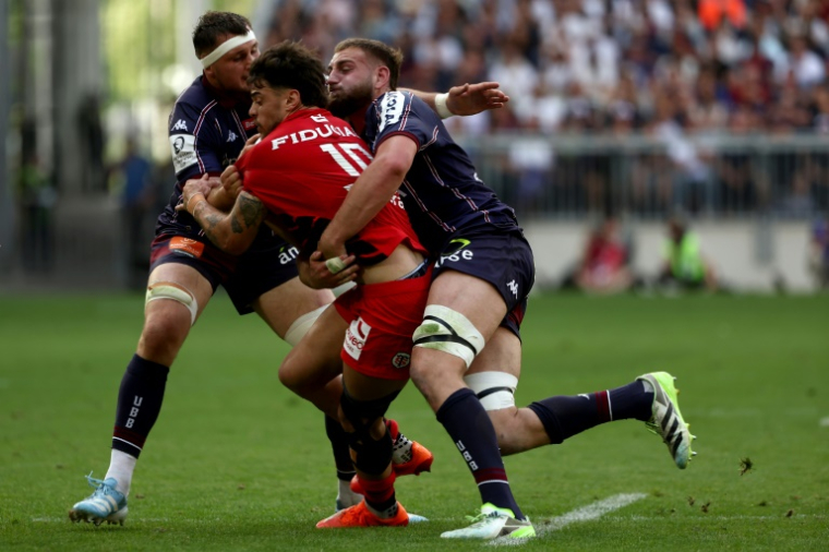 Le demi d'ouverture de Toulouse Romain Ntamack (centre) plaqué par les Bordelais Bastien Vergnes Taillefer (gauche) et Pierre Bochaton (droite) lors de la demi-finale de Champions Cup, le 4 mai 2025 à Bordeaux ( AFP / ROMAIN PERROCHEAU )