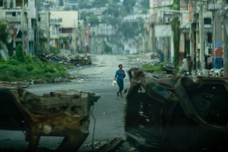 Une personne marche entre des carcasses de voitures brûlées, le 16 janvier 2026 à Port-au-Prince, en Haïti ( AFP / Clarens SIFFROY )