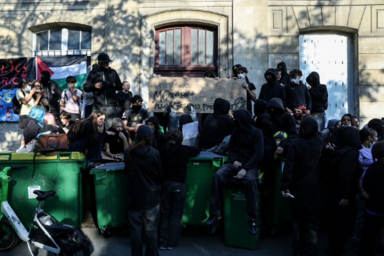 Des manifestants se tiennent debout sur des poubelles empilées à l'entrée du lycée Arago à Paris, le 29 septembre 2026 ( AFP / Kenzo TRIBOUILLARD )