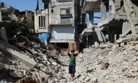 Un déplacé palestinien transportant un carton d'aide humanitaire marche au milieu de destructions à Nousseirat dans le centre de la bande de Gaza, le 19 octobre 2025 ( AFP / Eyad BABA )