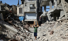 Un déplacé palestinien transportant un carton d'aide humanitaire marche au milieu de destructions à Nousseirat dans le centre de la bande de Gaza, le 19 octobre 2025 ( AFP / Eyad BABA )