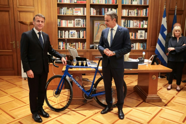Le président français Emmanuel Macron (G) offre un vélo produit en France au Premier ministre grec Kyriakos Mitsotakis à l'issue d'un déjeuner de travail, le 25 avril 2026 à Athènes  ( AFP / Ludovic MARIN )
