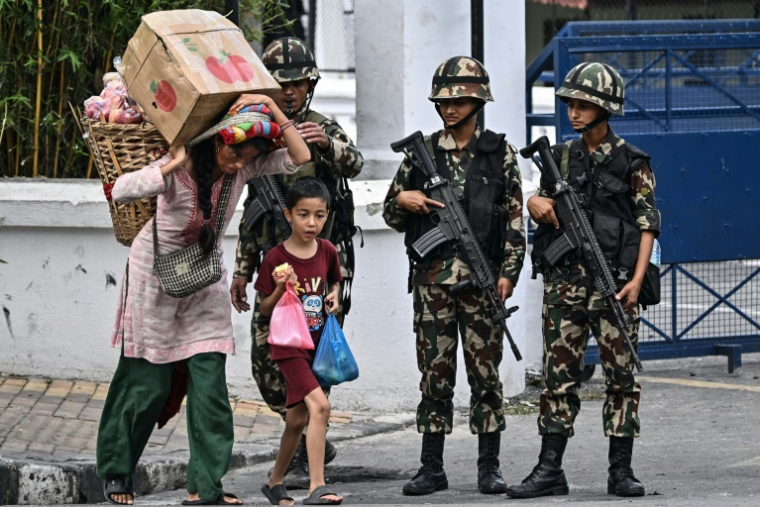 Une habitante, chargée de fruits et légumes, passe avec un enfant devant des soldats aux heures autorisées pendant un couvre-feu imposé pour rétablir la loi et l'ordre à Katmandou, le 12 septembre 2025 au Népal ( AFP / Pedro Pardo )