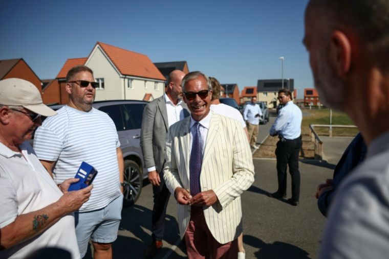 Nigel Farage, (c) chef du parti britannique Reform UK, parle avec des électeurs à la sortie d'un bureau de vote installé dans une école primaire de Walton-on-the-Naze, dans l'Essex, lors de l'élection partielle de Clacton, le 13 août 2026 ( AFP / Henry NICHOLLS )