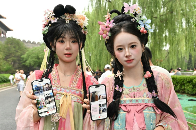 Des touristes originaires de la province de Jilin, dans le nord-est de la Chine, montrent leurs comptes Xiaohongshu sur leurs téléphones alors qu'elles visitent la Cité interdite à Pékin, le 11 juillet 2026 ( AFP / ADEK BERRY )