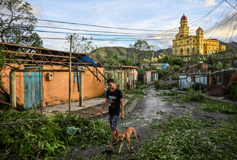 Un habitant d'El Cobre, dans la province de Santiago de Cuba, promène son chien parmi des arbres et des lignes électriques tombés à terre, ainsi que des maisons détruites après le passage de l'ouragan Melissa, le 29 octobre 2025 ( AFP / YAMIL LAGE )